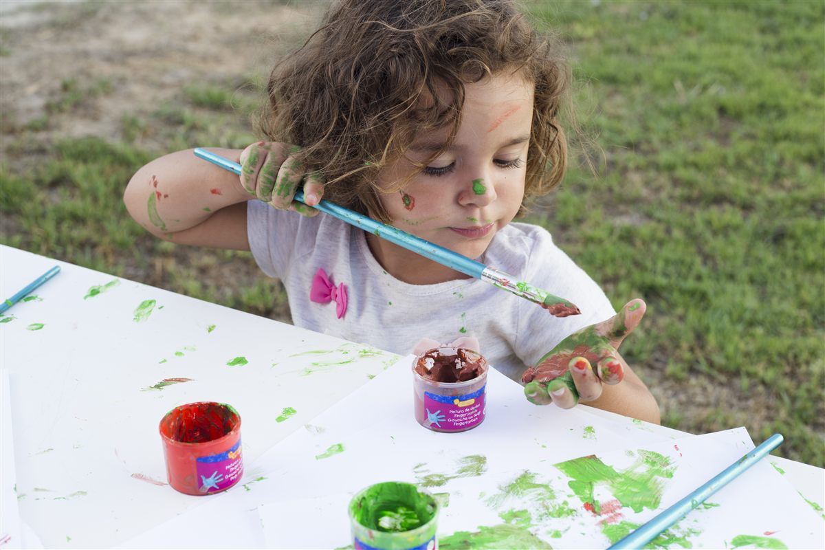Peque pintando con pincel y pintura de dedos en una mesa al aire libre